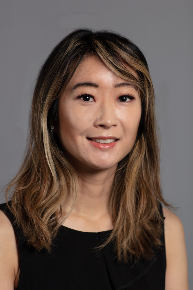 Headshot of Jenny Zhao wearing a black sleeveless dress shirt on a gray background.